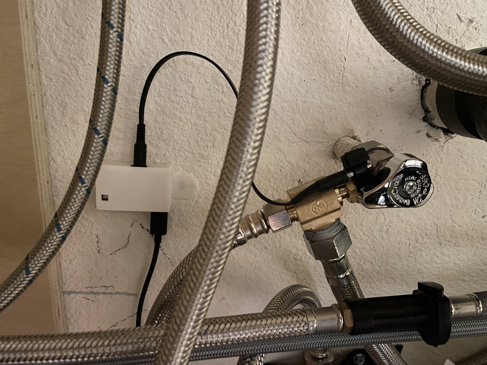 An Apollo TEMP-1 zip-tied to the hot-water angle stop under the sink, its probe clamped to the valve.