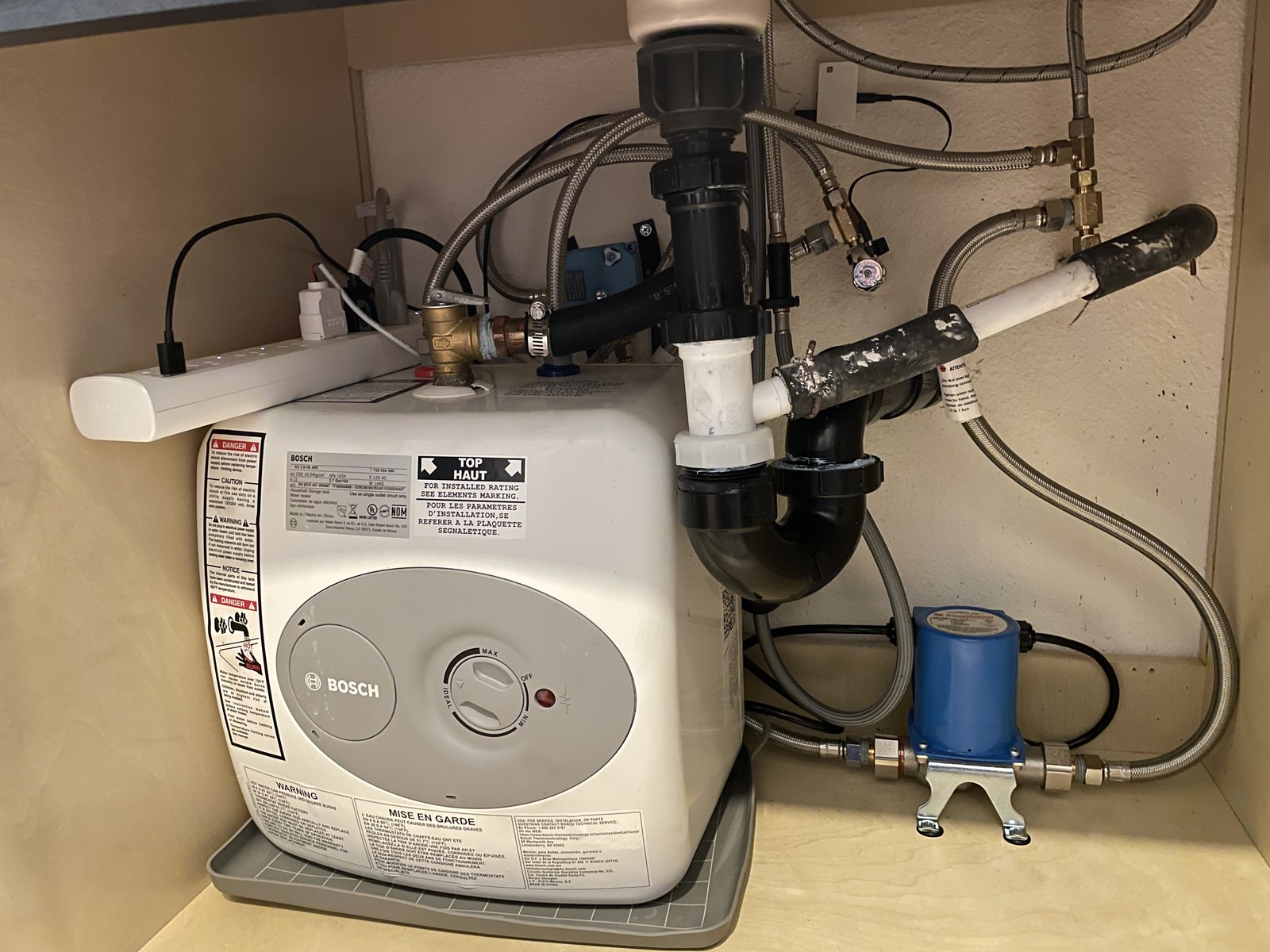 Under-sink install showing a Bosch mini tank with a smart power strip on top, a 3-way motorized valve on the wall, and a circulator pump bolted to the floor.